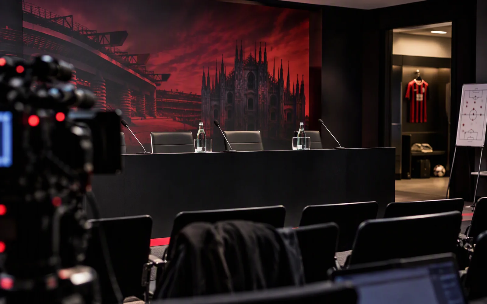 Press room with microphones in front of a mural of San Siro and the Duomo
